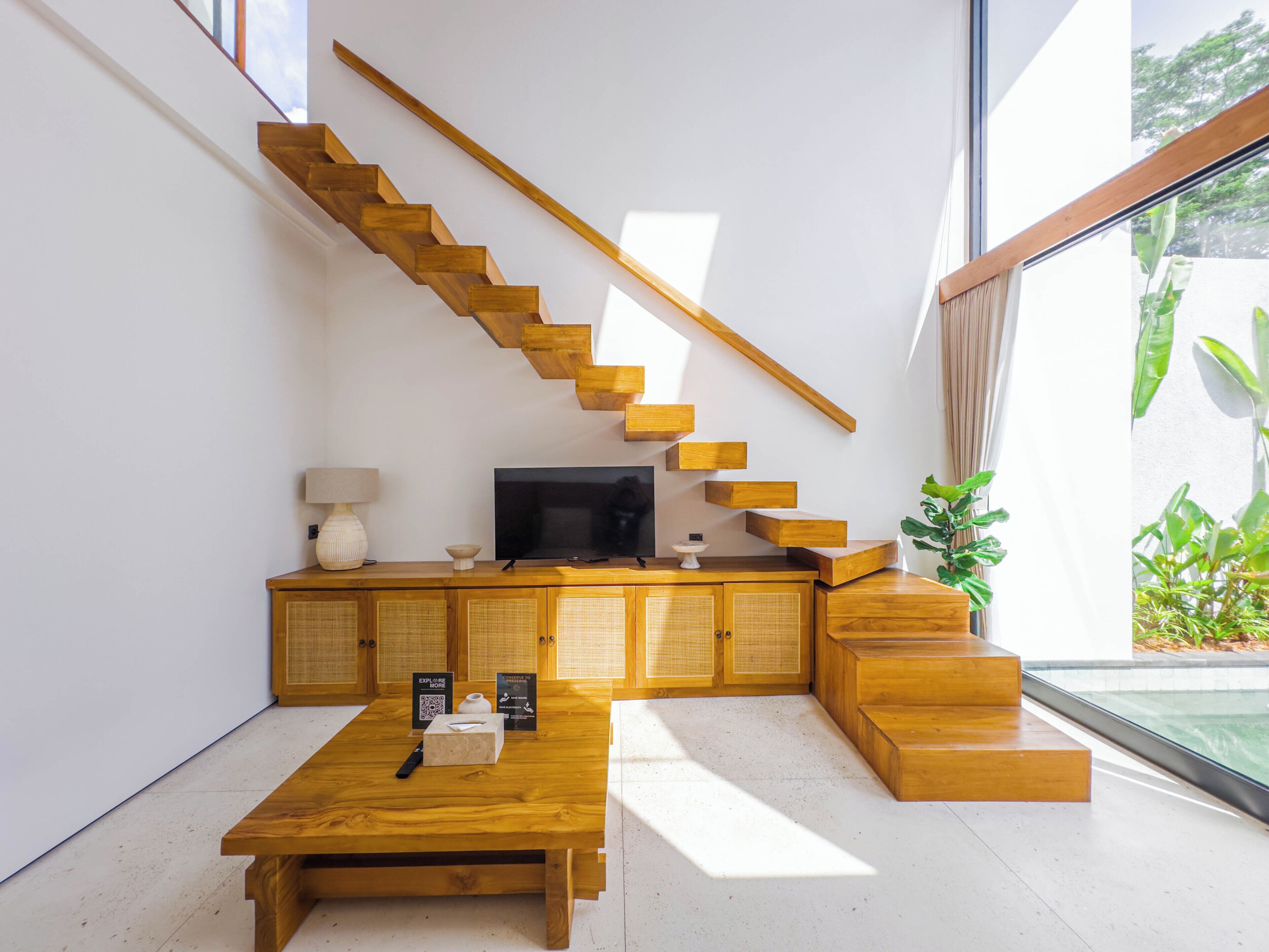 Un interior moderno con una escalera de madera, un televisor de pantalla plana y una mesa de centro de madera.
