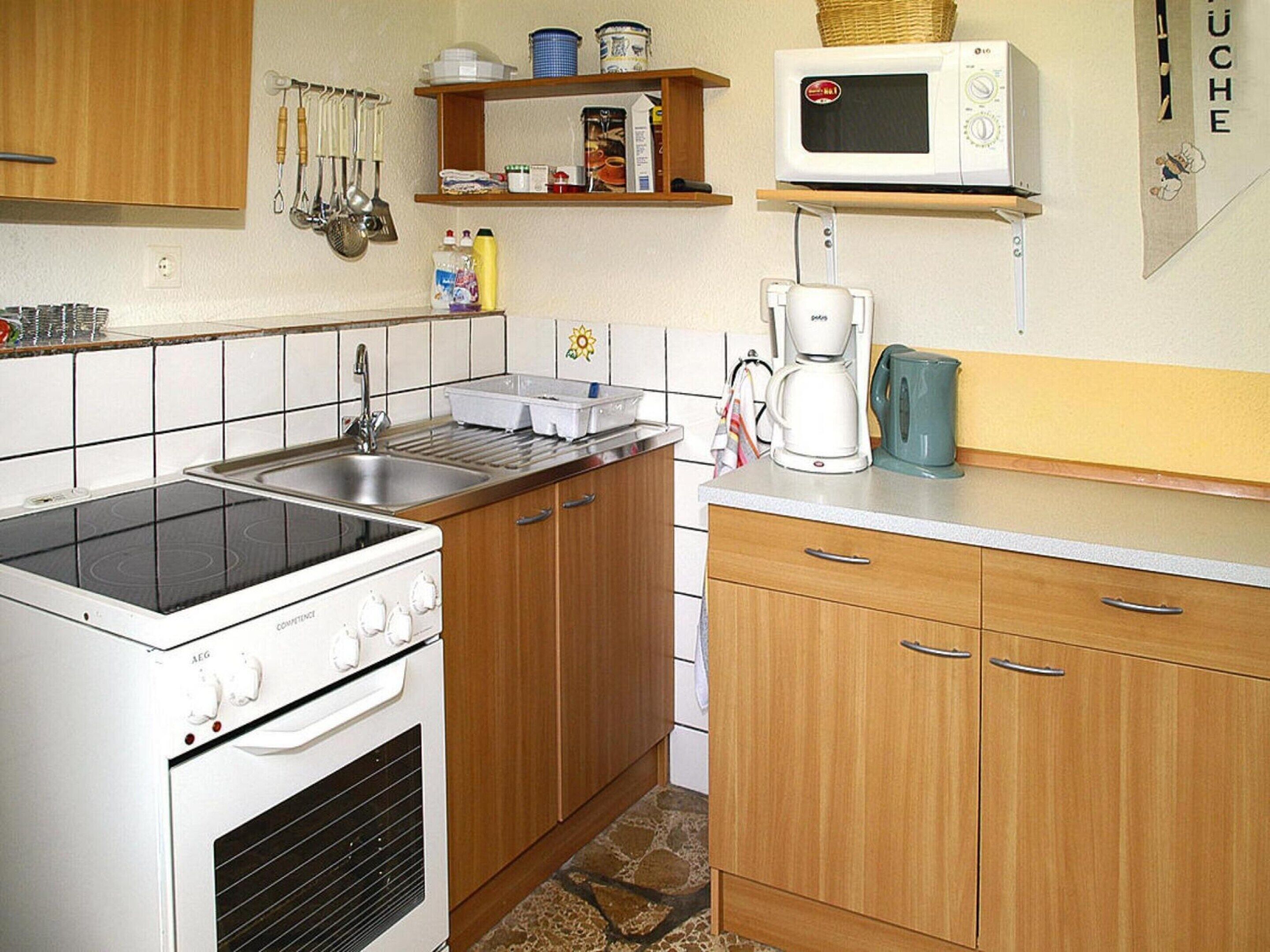 Een kleine keuken met een kookplaat, magnetron, koffiezetapparaat en houten kastjes.