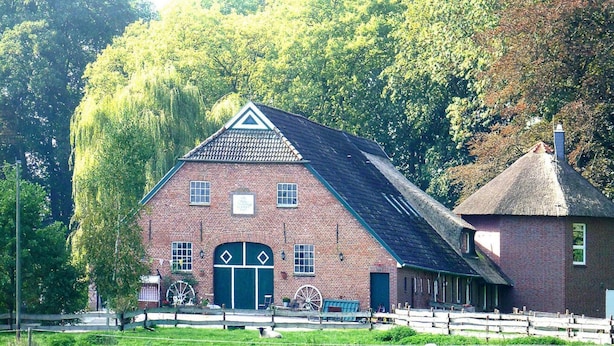 A traditional brick building with a thatched-roof annex, surrounded by a wooden fence and lush greenery. - Ferienhof Landhaus Markus, Suderschwei (Stadland)