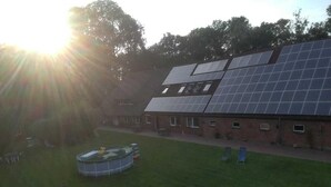 A building with a large solar panel array on the roof, a swimming pool, and a boat in the yard. - Ferienhof Landhaus Markus, Suderschwei (Stadland)
