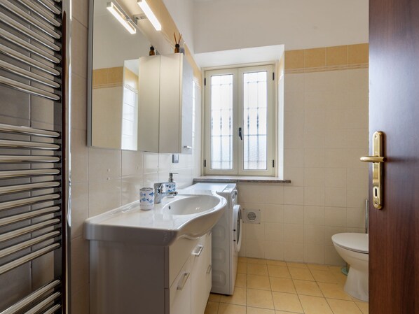 A bathroom with a white sink, a mirror, a window, and a toilet.