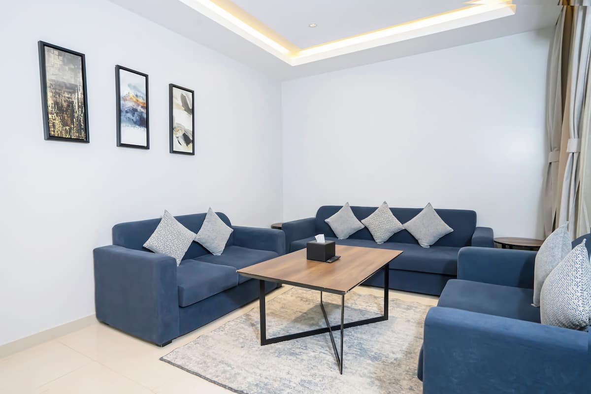 Een moderne woonkamer met twee blauwe banken, een houten salontafel en drie ingelijste kunstwerken aan de muur.