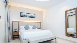 Una habitación de hotel moderna con una cama grande, mesitas de noche, un banco, una obra de arte con un paisaje urbano y un espejo.
