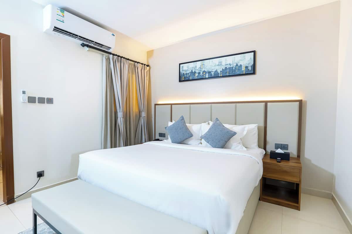 Een moderne hotelkamer met een groot bed, een nachtkastje met een lamp, en een stadsgezicht op de muur.