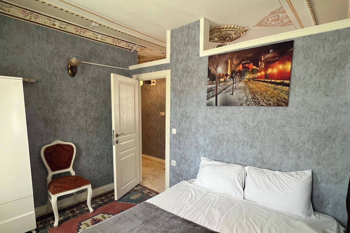 A bedroom with a large bed, a chair, a wardrobe, and a door leading to another room.