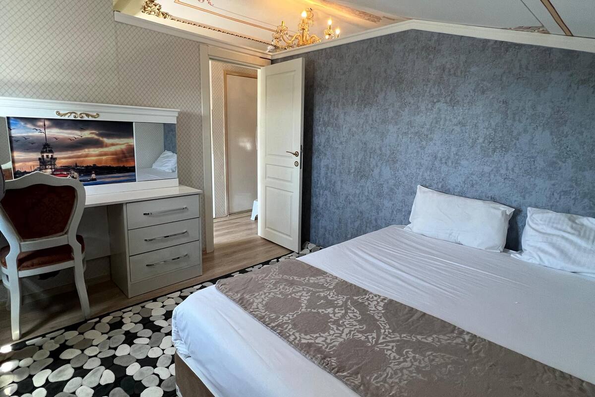 A bedroom with a bed, a desk, and a chair. There is a door leading to another room.