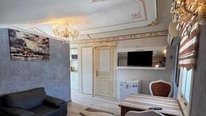 A living room with a sofa, a dining table with chairs, a TV, and a patterned rug. - Mihri Hatun Suit Otel (Istanbul)