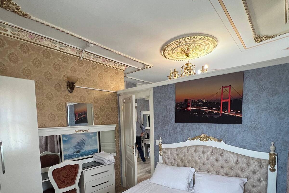 A hotel room with a bed, a desk with a chair, a wardrobe, and a painting of a bridge.