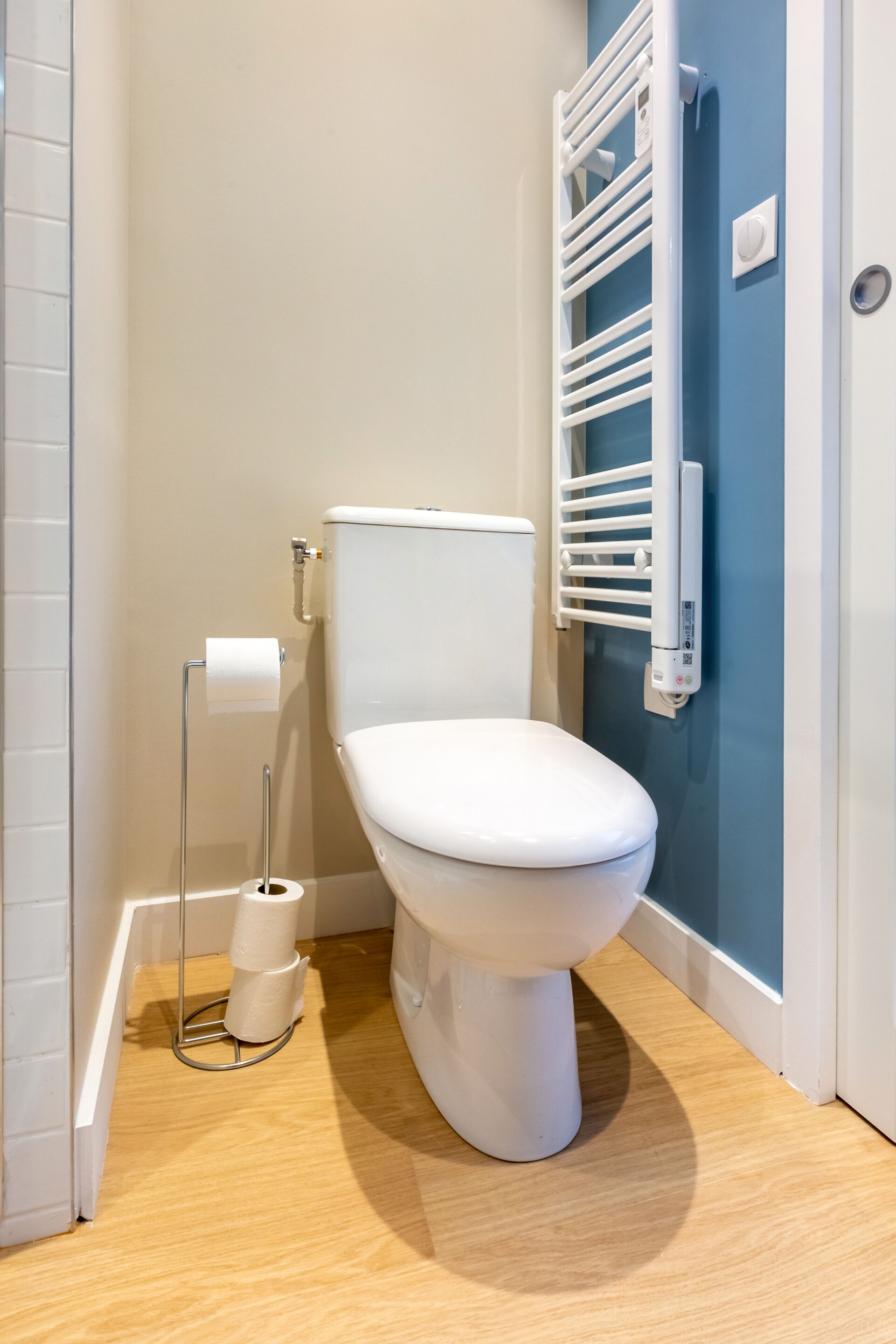 Um banheiro moderno com vaso sanitário branco, porta-papel higiênico e porta-toalhas.