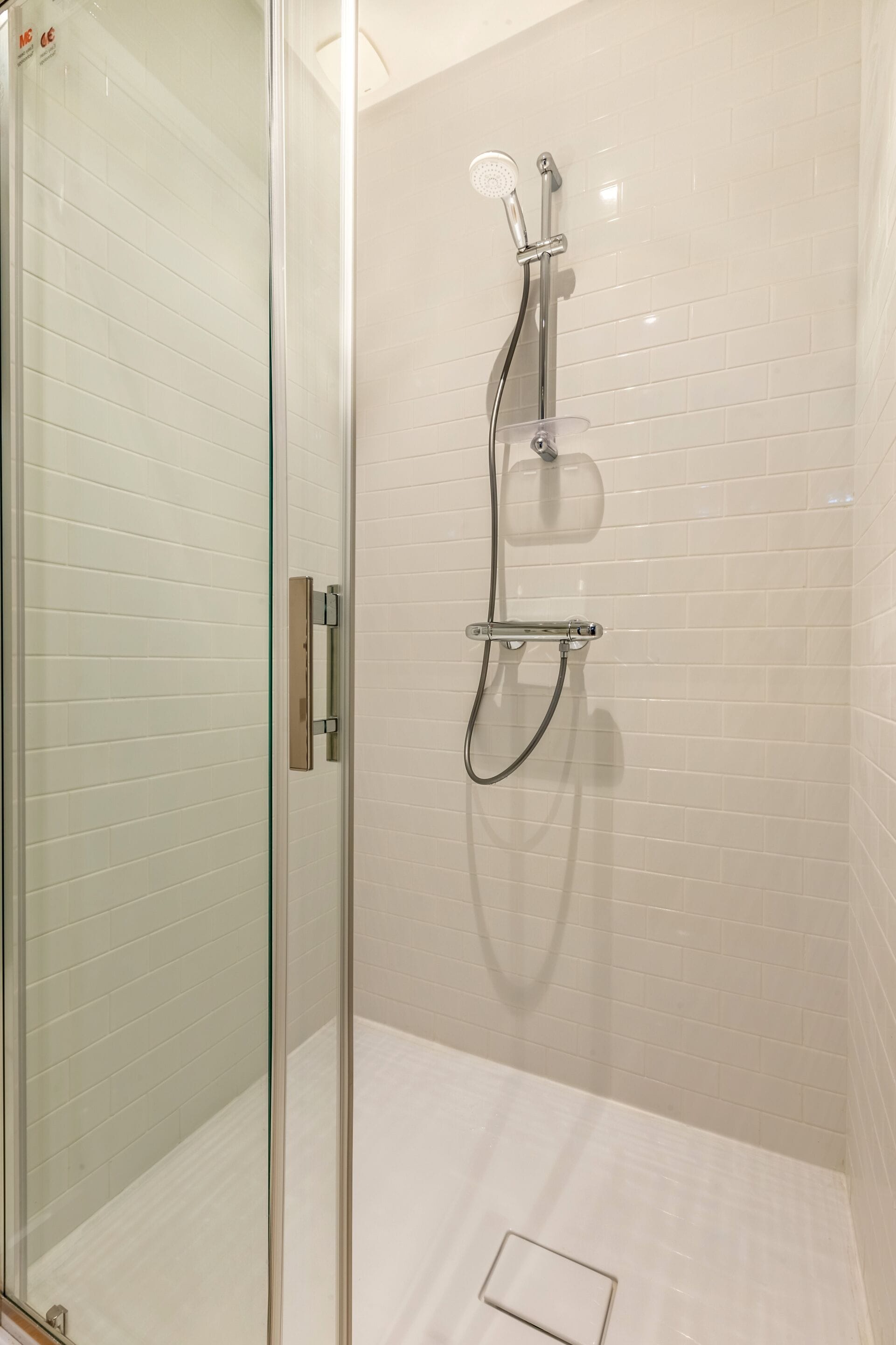 Een douchecabine van glas met een handdouche en een kraan op de muur.