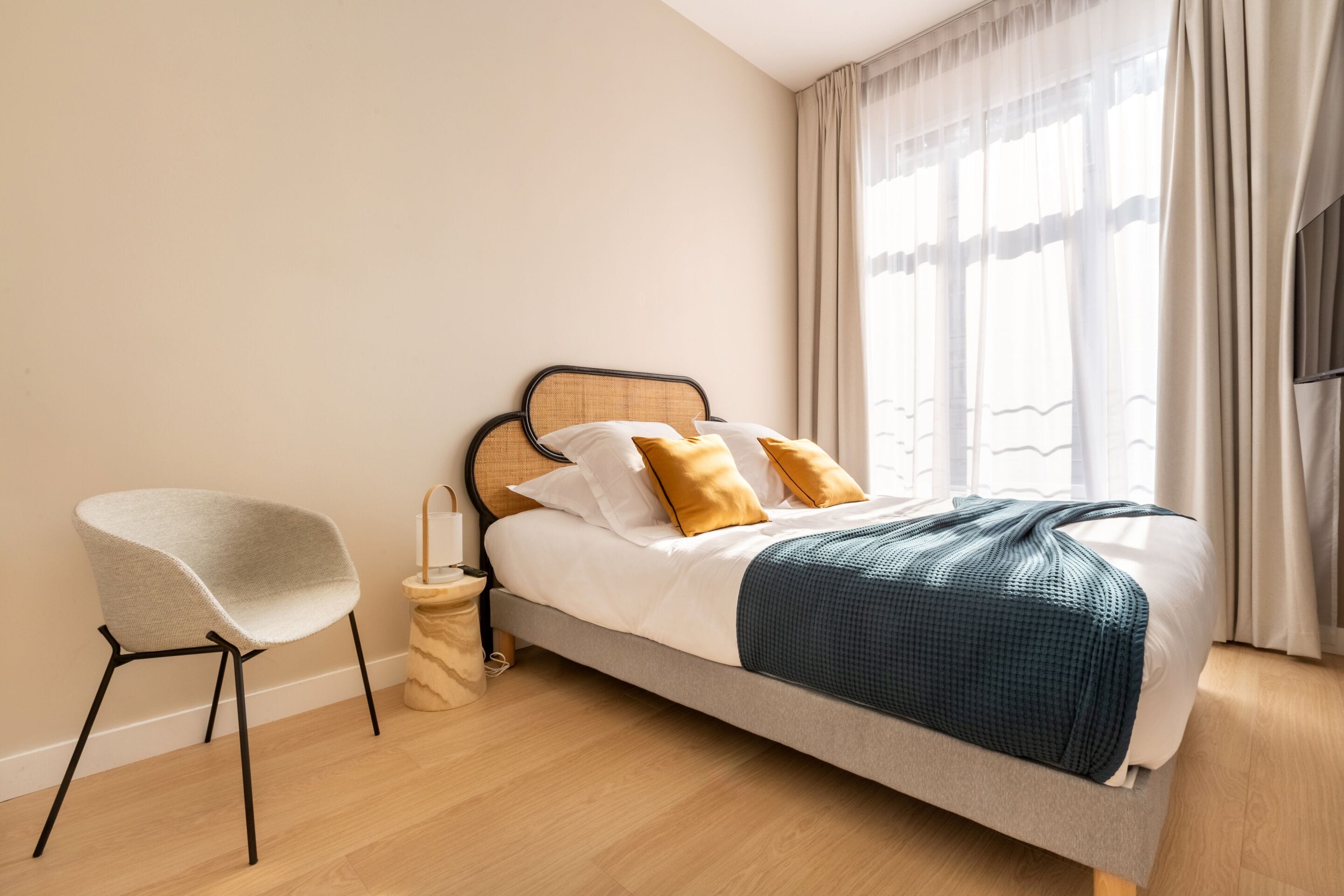 A modern bedroom with a bed, a chair, and a bedside table.