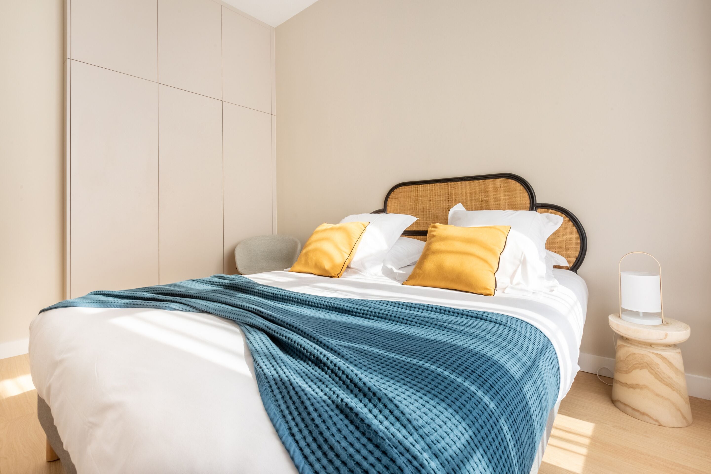 A neatly made bed with a blue and white striped blanket, two yellow pillows, and a wooden bedside table with a white lamp.