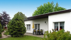 A two-story white building with a black roof, a small patio with a table and chairs, and a large evergreen tree in the foreground. - Twin Bungalow at Black Lake, Schwarz (Schwarz)