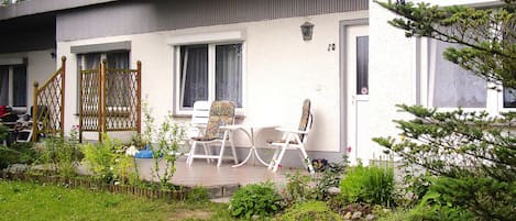 A white building with a covered porch, two white chairs, and a wooden gate.