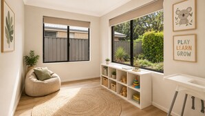 A room with a bean bag chair, a bookshelf, a window with a view of a garden, and a play area with a sign. - The Aurora (Geographe)