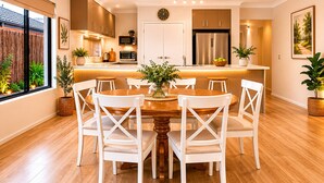 A modern kitchen with white cabinetry, a central island, and a dining area with white chairs. - The Aurora (Geographe)