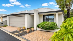 A modern two-story house with a garage, a brick driveway, and a well-maintained garden with various plants and flowers. - The Aurora (Geographe)