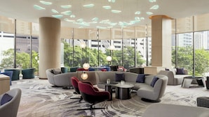 A modern lounge area with sofas, chairs, and tables, large windows offering views of the city, and a unique ceiling light design. - Holiday Inn Kuala Lumpur Bangsar (Kuala Lumpur)