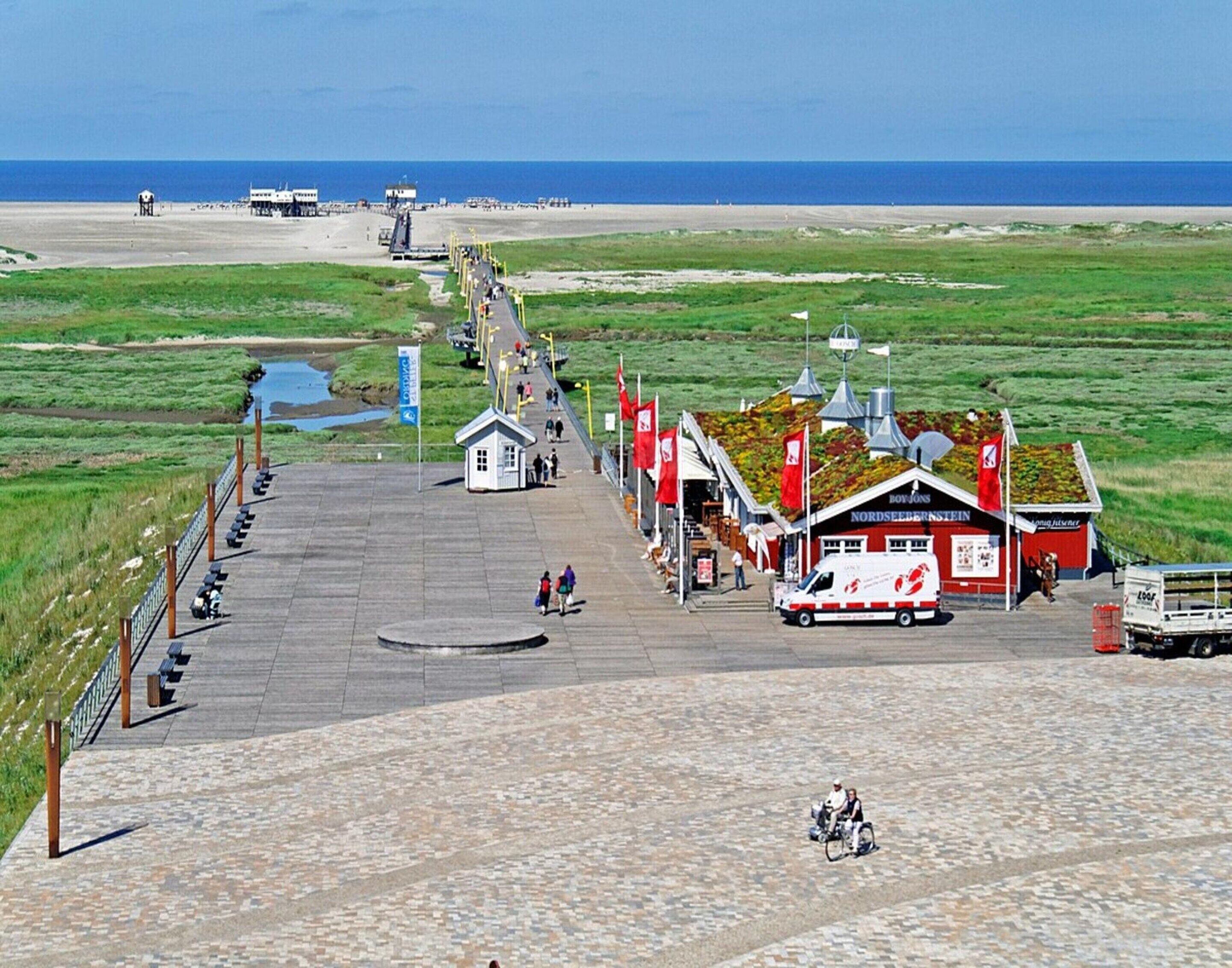 A coastal area with a paved walkway leading to a building with a red facade, a small kiosk, and a boat ramp.