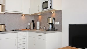 A modern kitchen with white cabinets, a microwave, a coffee maker, and a Samsung TV on a wooden table. - Ferienwohnung, St. Peter-ording (St. Peter-Ording)