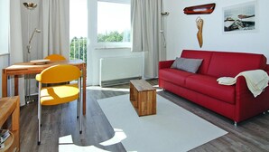 A living room with a red sofa, a wooden coffee table, a yellow chair, and a dining table with a lamp. - Ferienwohnung, St. Peter-ording (St. Peter-Ording)