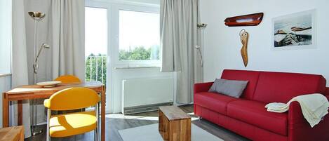 A living room with a red sofa, a wooden coffee table, a yellow chair, and a dining table with a lamp.