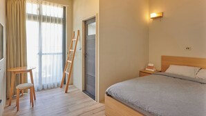 Une chambre d’hôtel comprenant un lit, une table de chevet, une chaise, une échelle en bois, une fenêtre avec des rideaux et un luminaire fixé au mur.