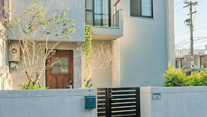 Une maison moderne à deux étages, dotée d’un toit plat, d’un balcon et d’une porte d’entrée.