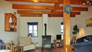 A living room with a wooden ceiling, a fireplace, a sofa, a television, and a dining area with a table and chairs. - Ferienhaus im Hafendorf Vieregge (Neuenkirchen)