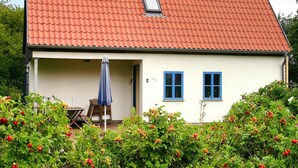A house with a red tiled roof, a small window, and a door leading to a porch with a table and an umbrella. - Ferienhaus im Hafendorf Vieregge (Neuenkirchen)