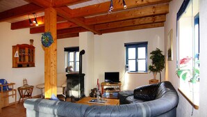 A cozy living room with a leather sofa, a wooden ceiling, a fireplace, and a television. - Ferienhaus im Hafendorf Vieregge (Neuenkirchen)