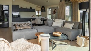 Een moderne woonkamer met een grijze modulaire bank, een ronde salontafel en rieten meubels.