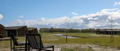 Eine Holzterrasse mit Stuhl und Tisch, ein kleiner Teich und eine Reihe von Hütten im Hintergrund.
