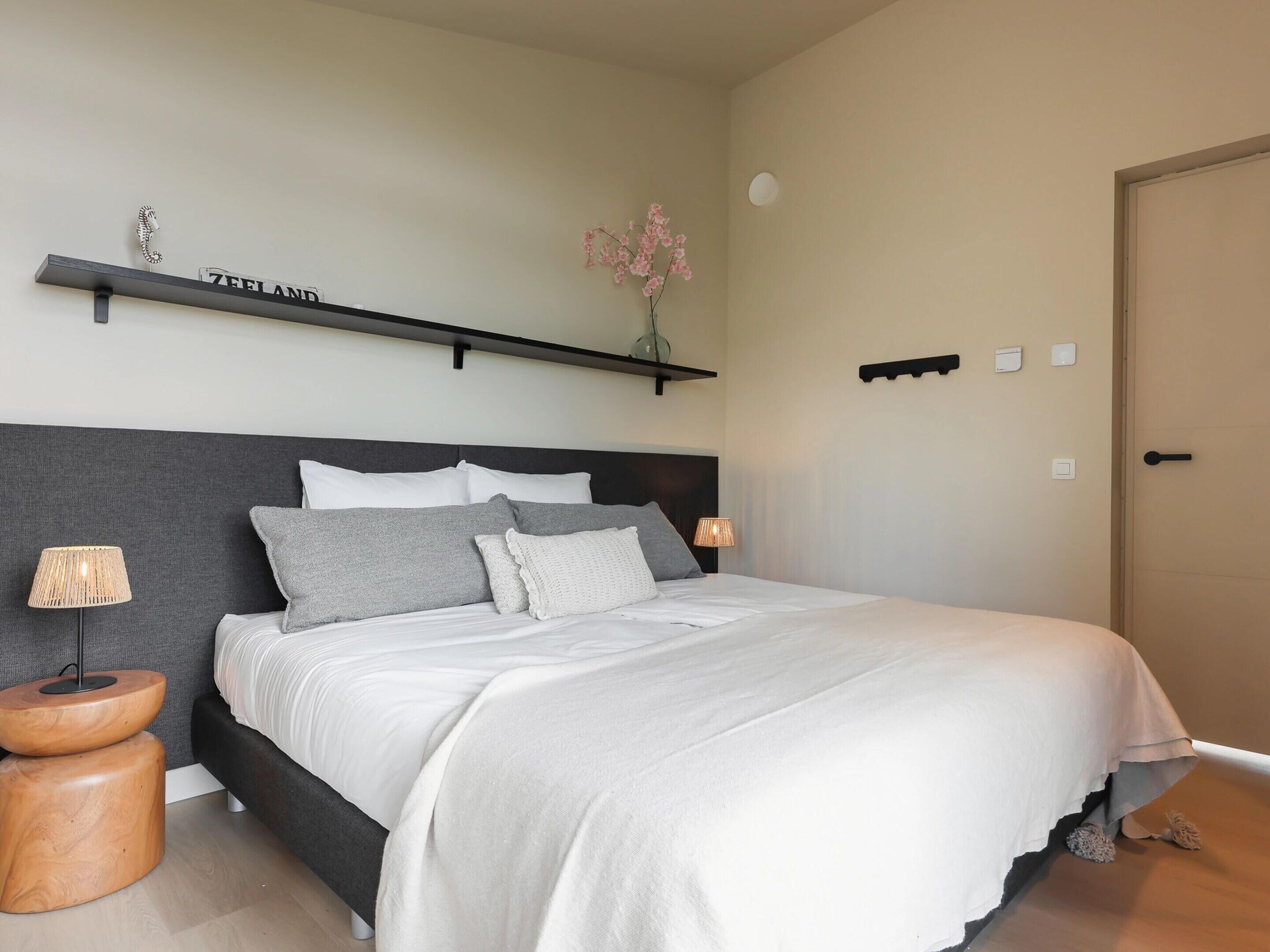 A bedroom with a bed, bedside tables, a wall-mounted shelf with a sign, and a door.