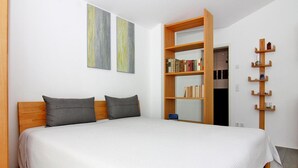 A bedroom with a large bed, a wooden headboard, two gray pillows, a wooden nightstand, a bookshelf, and a mirror. - Appartementhaus Calmsailing, Borgerende (Boergerende-Rethwisch)