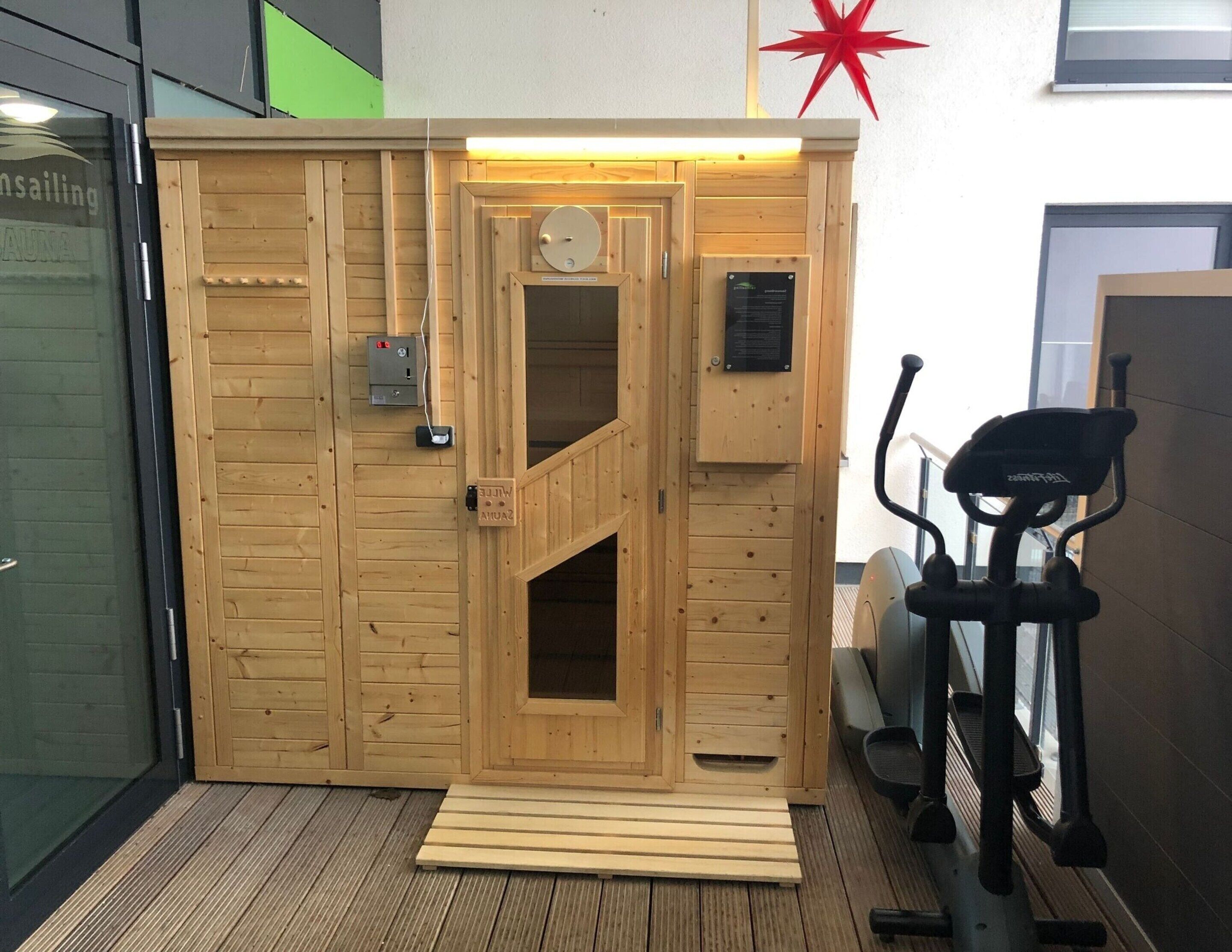 A sauna room with wooden walls, a door, a control panel, and a treadmill.