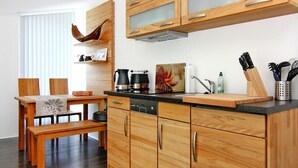 A modern kitchen with wooden cabinets, a black countertop, and a dining area with a wooden table and bench. - Appartementhaus Calmsailing, Borgerende (Boergerende-Rethwisch)