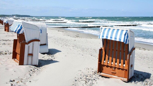 Beach chairs with striped canopies on a sandy beach with waves in the background. - Appartementhaus Calmsailing, Borgerende (Boergerende-Rethwisch)