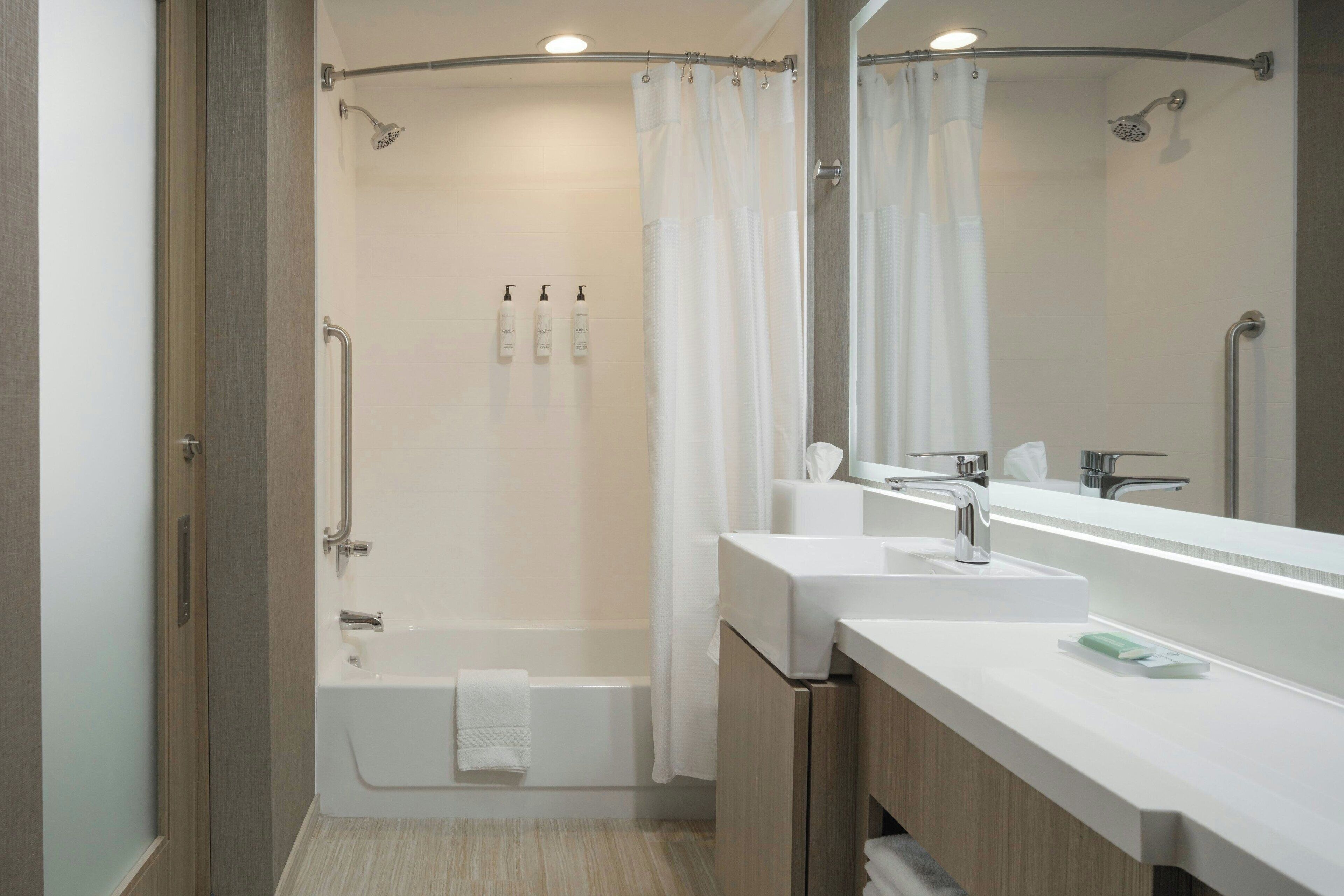 Un baño moderno con ducha, dos lavamanos, un espejo grande y un perchero para toallas.