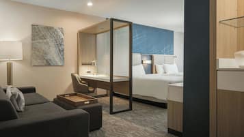 A modern hotel room with a bed, a desk, a chair, a sofa, and a large mirror.