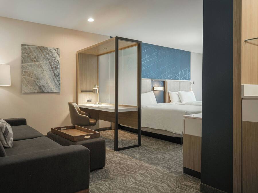 A modern hotel room with a bed, a desk, a chair, a sofa, and a large mirror.
