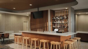 A bar area with wooden stools, a counter with a TV, and shelves of liquor bottles. - SpringHill Suites by Marriott Lexington Frankfort (Frankfort)