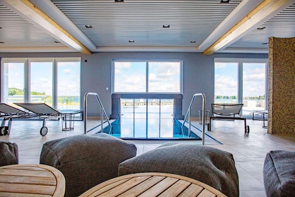 A spacious indoor area with a pool, seating, and large windows offering views of the outdoors.