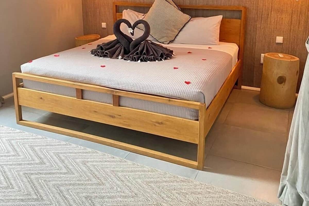 Un dormitorio moderno con una cama de madera, dos lámparas fijadas a la pared y un adorno con forma de corazón sobre la cama.