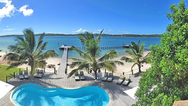 Un área de piscina con sillones de descanso, una terraza de madera y vistas a la playa y al océano.