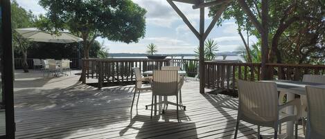 Una terraza de madera con mobiliario exterior, un área cubierta y vistas al agua.