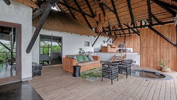 Un espacio exterior amplio con una terraza de madera, una estructura de techo de paja, un sofá de mimbre y una pequeña piscina.