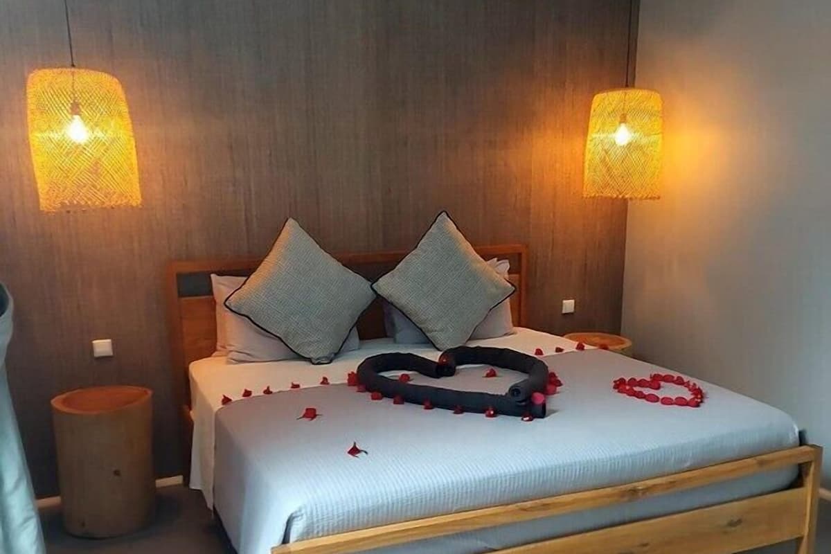 Un dormitorio con cabecera de cama de madera, dos lámparas de noche, una mesita de noche y un cubo de basura pequeño.