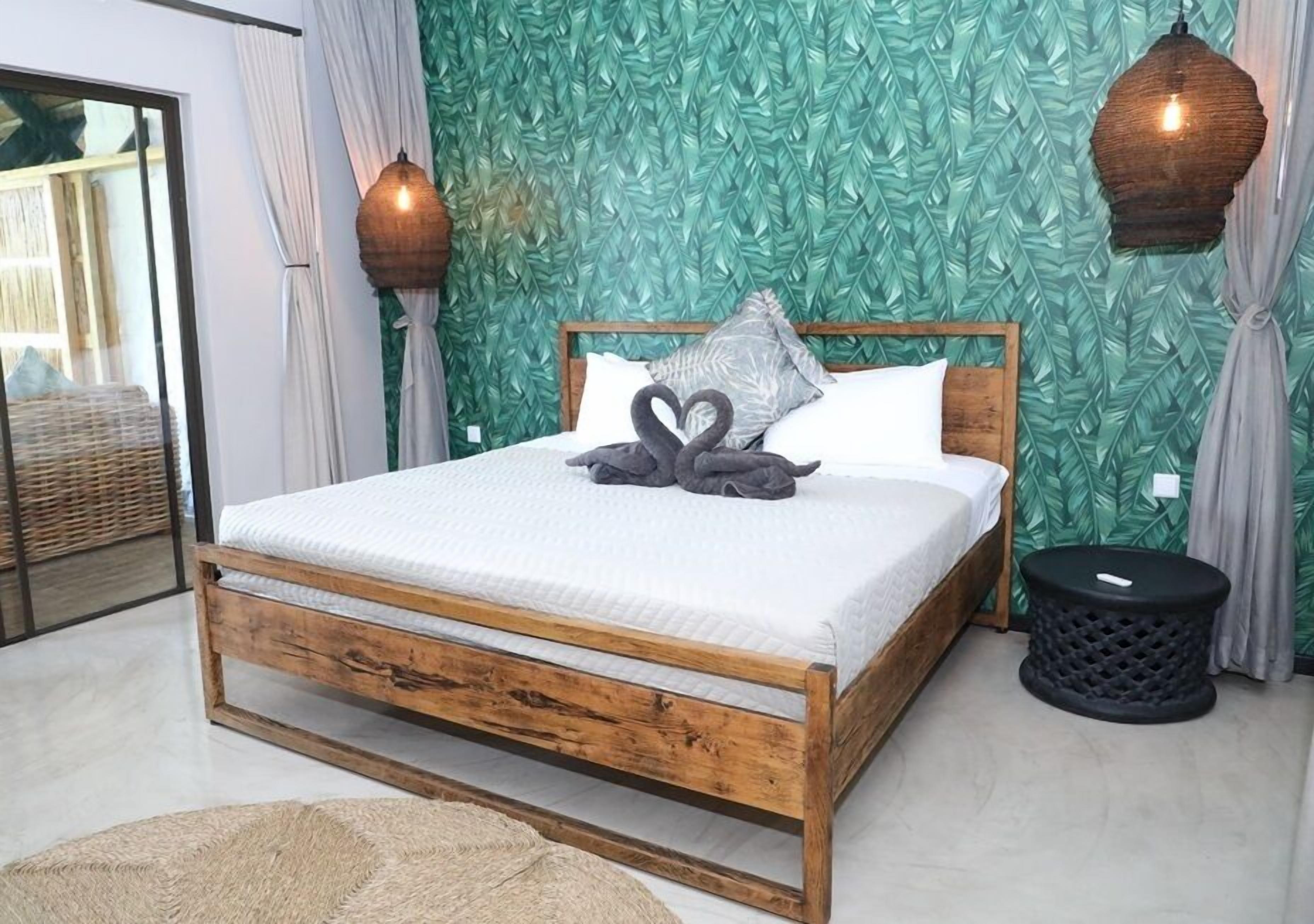 A wooden bed with a white mattress, two pillows, and a swan-shaped pillow arrangement.