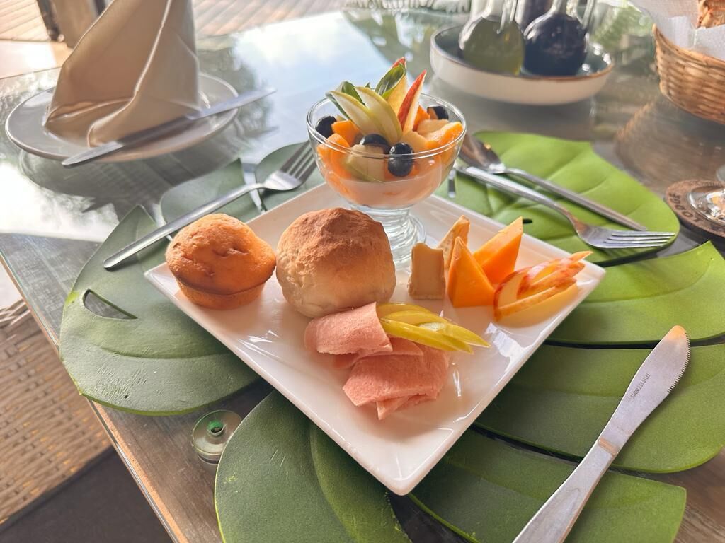 A breakfast setting with a glass bowl of fruit salad, two pastries, and sliced fruit on a plate.